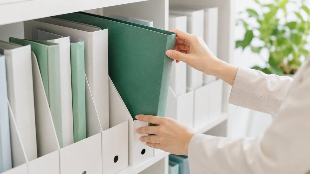 ファイル棚に緑のファイルを収める手元